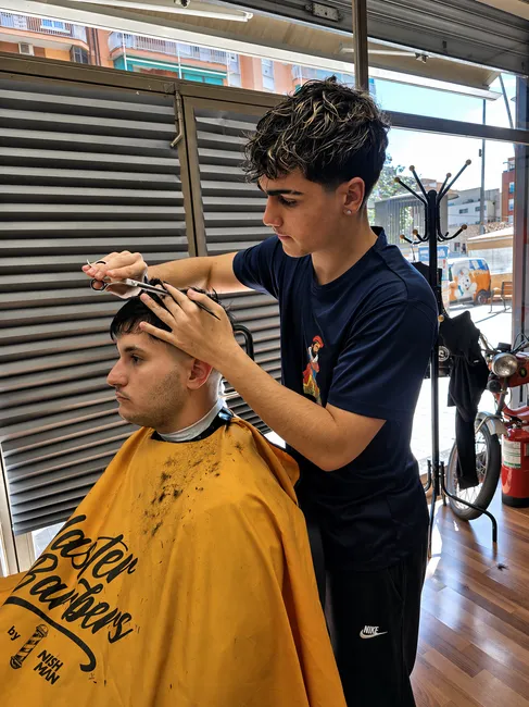 Un barbero trabaja con tijeras y peine en la parte superior del cabello de un cliente.